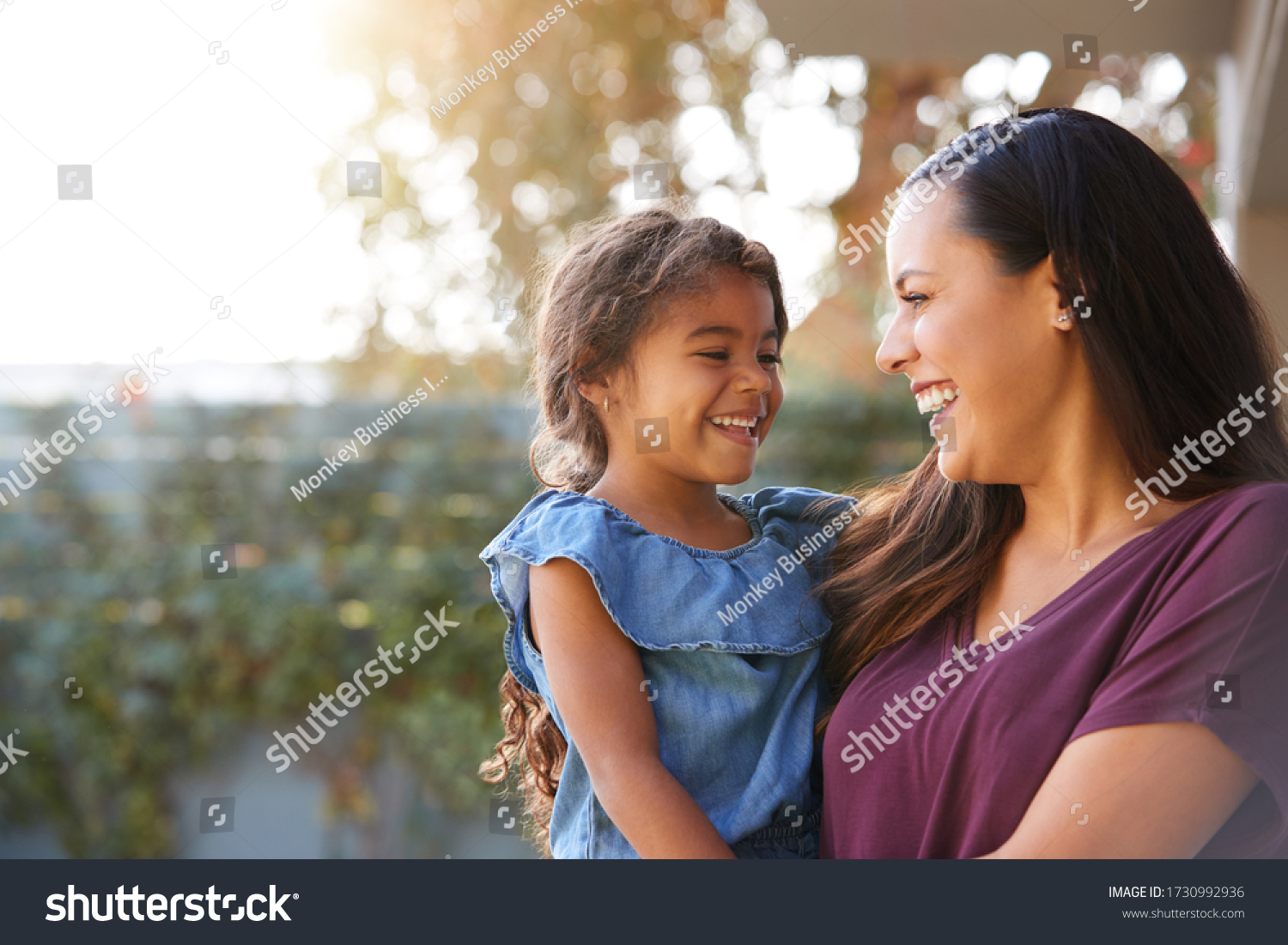 Smiling Hispanic Mother Holding Daughter Laughing In Garden At Home #1730992936