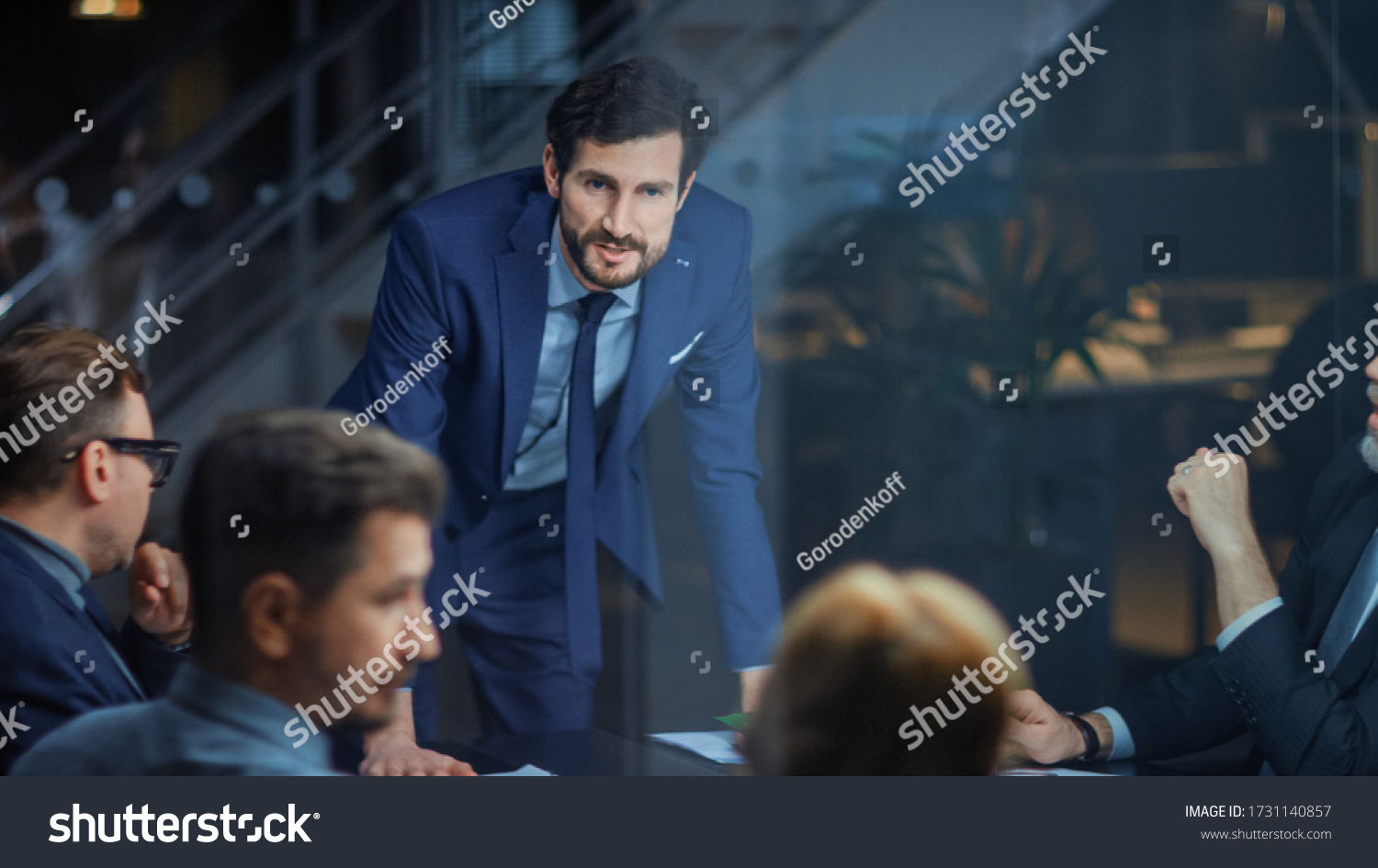Corporate Meeting Room: Confident and Handsom Executive Director Decisively Leans on a Conference Table and Delivers Report to a Board of Executives about Company’s Record Breaking Revenue #1731140857