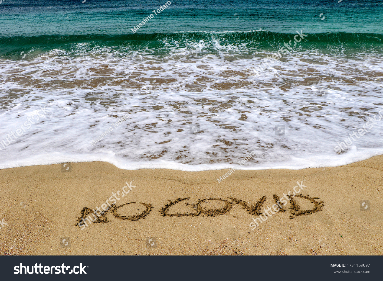 "No covid" written on the sand of the shore of a beach with incoming waves. Fear of beach resort managers for the upcoming summer season due to the coronavirus covid-19 #1731159097