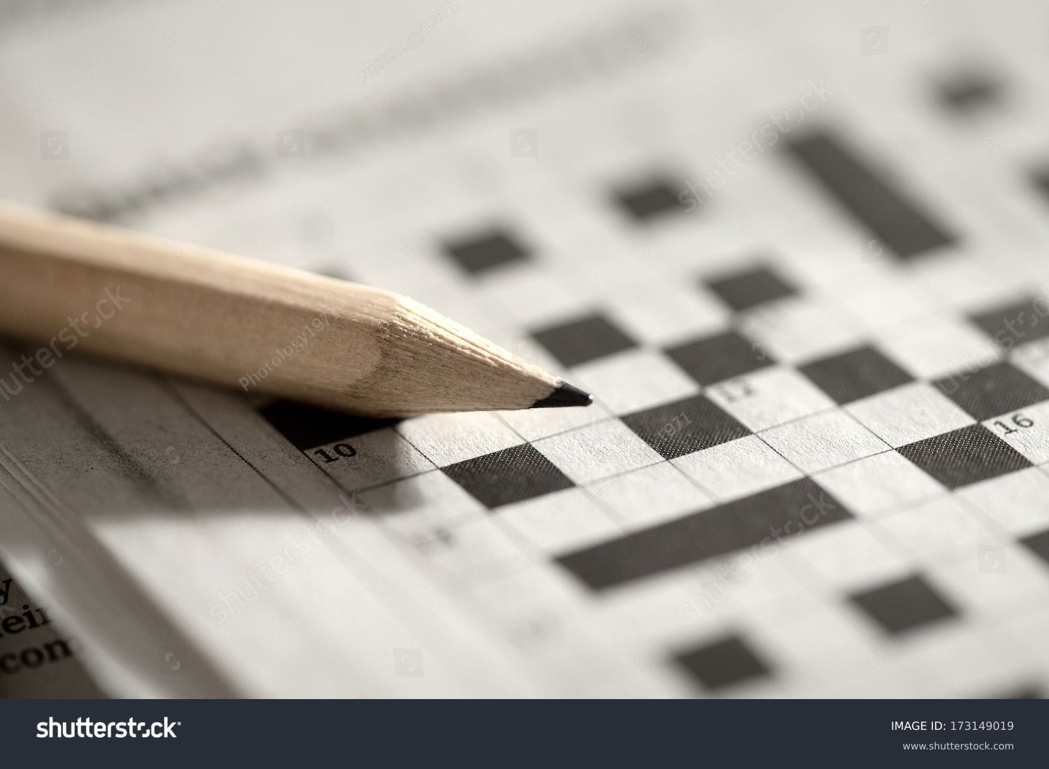 Close up view of a blank crossword puzzle grid with black and white squares and a pencil #173149019