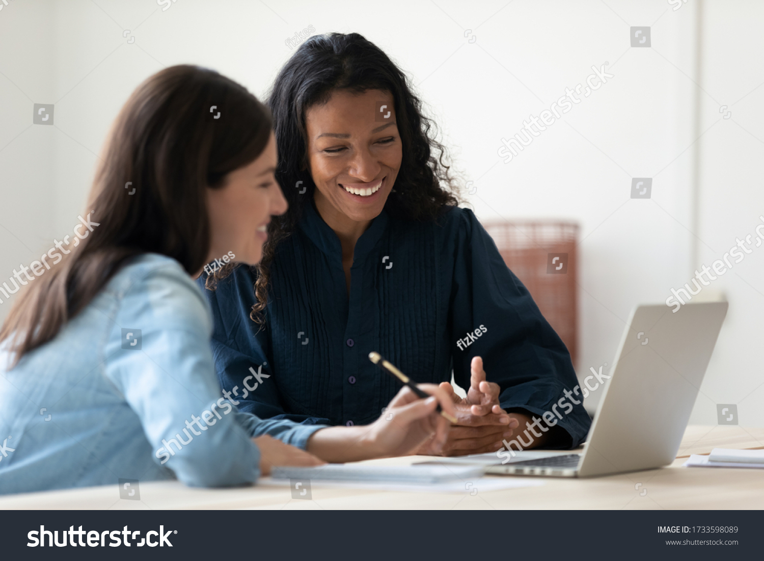 Close up happy young african american businesswoman using laptop with laughing female mentor in coworking boardroom at meeting. Smiling diverse woman managers talking about new business concept. #1733598089