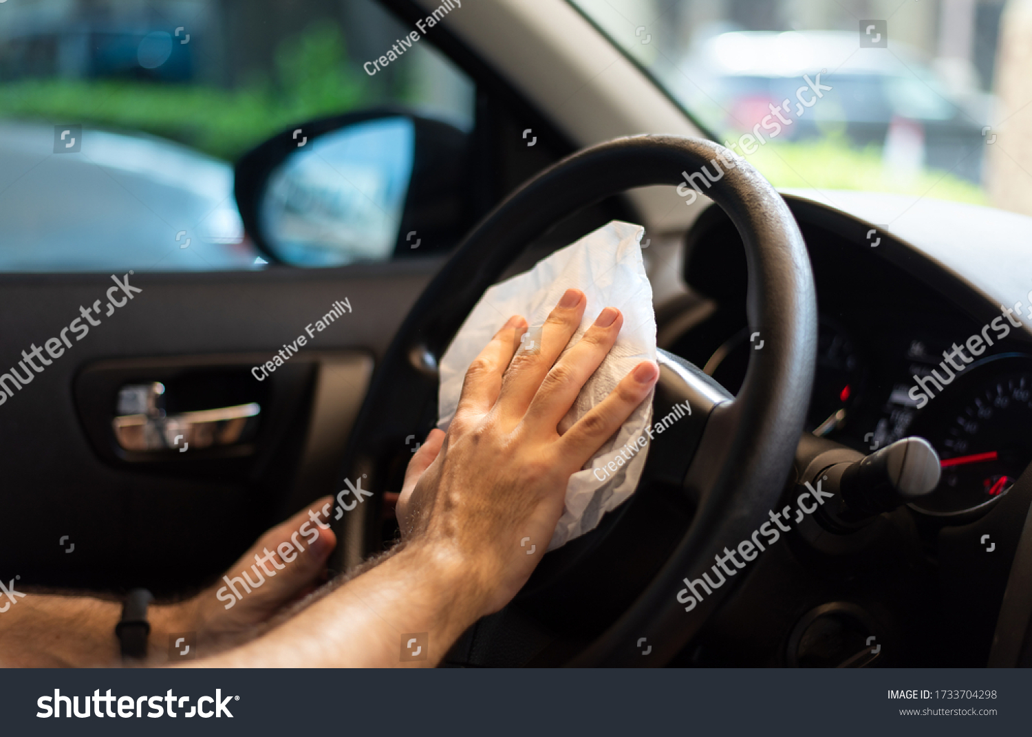 Man cleaning his car steering wheel for disinfection and a safe ride during the virus pandemic closeup