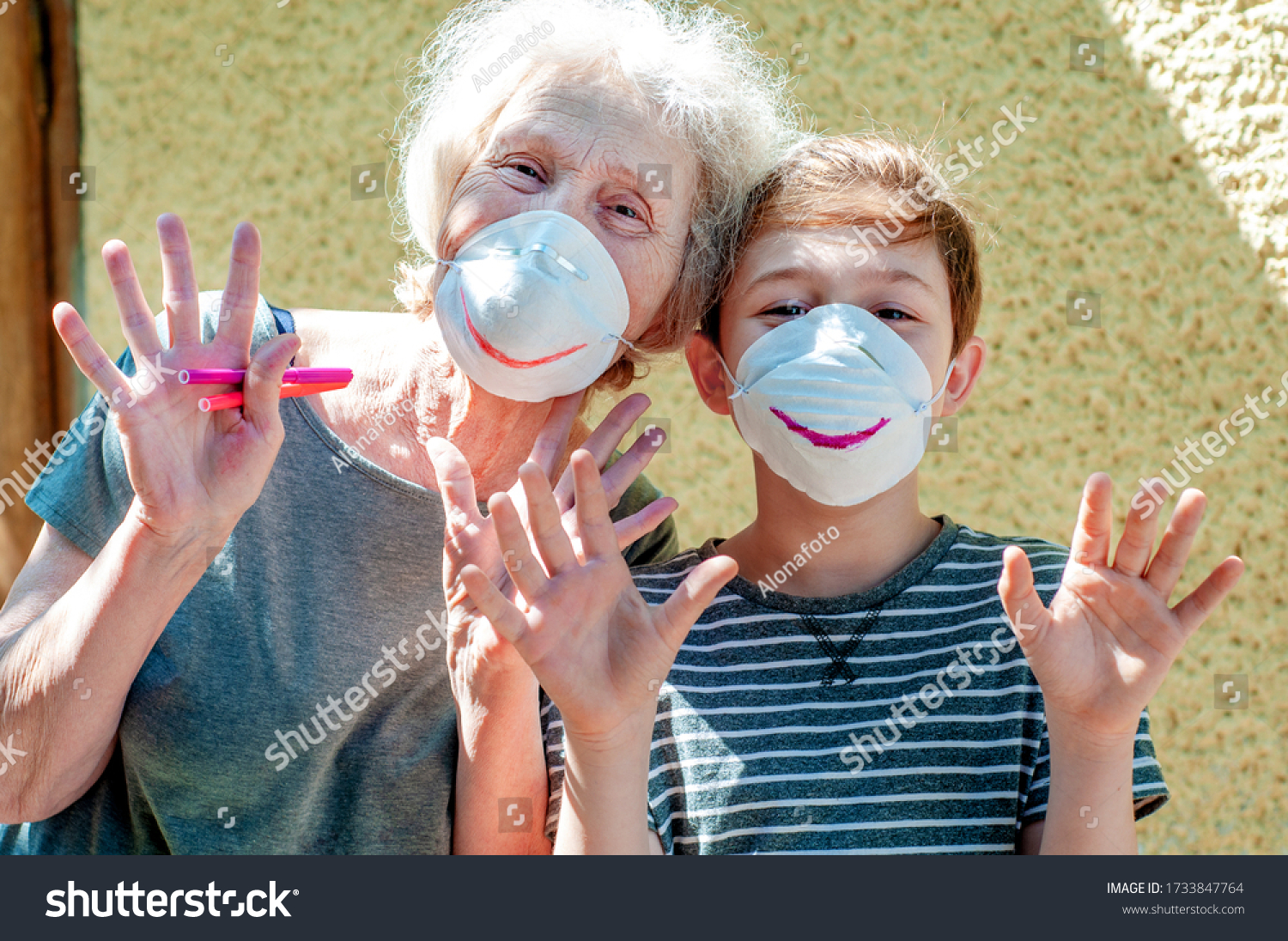 Happy laughing grandmother with grandchild in a respiratory masks plays together near house. Family fun. Stay at home. Drawing a smile on protective masks. Quarantin, isolated. Coronavirus covid-19. #1733847764