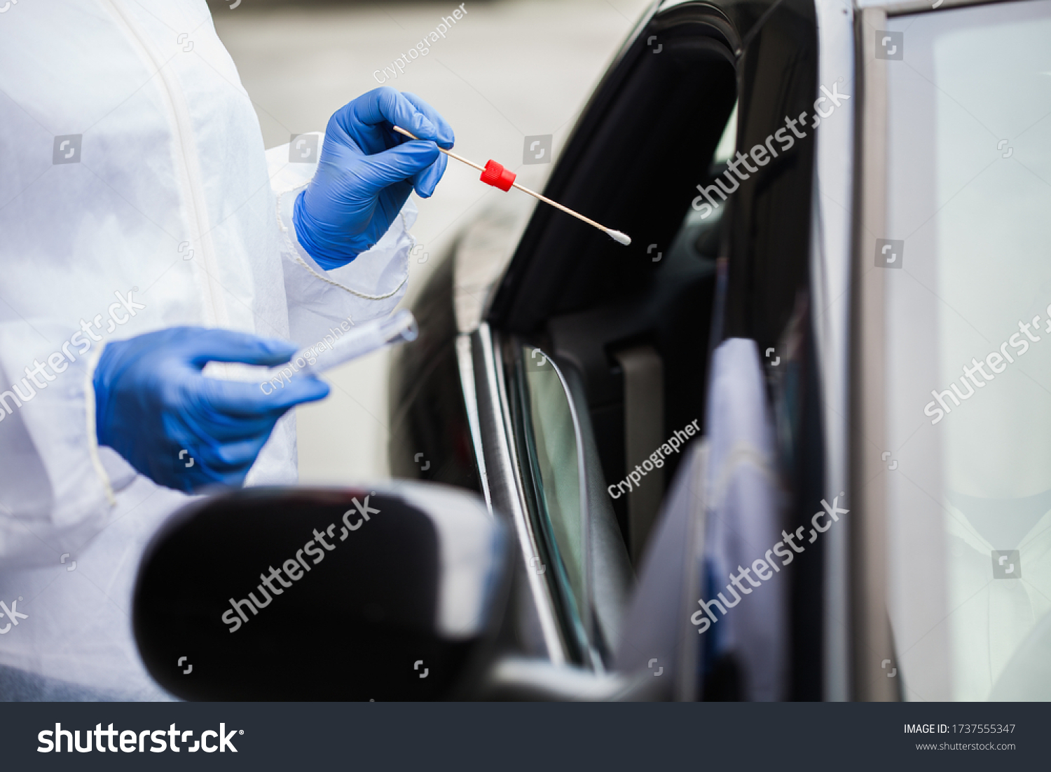 Medical worker in N95 PPE performing nasal throat swab on person in vehicle through car window,COVID-19 UK mobile testing centre drive thru facility,hands closeup in blue gloves holding test kit #1737555347