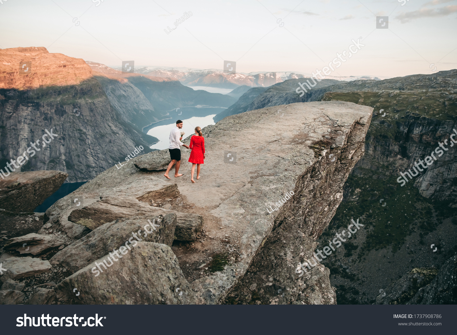 Young couple walking in troll tongue in norway in summer at sunset. Beautiful landscape, cliff, rocks, mountains. #1737908786