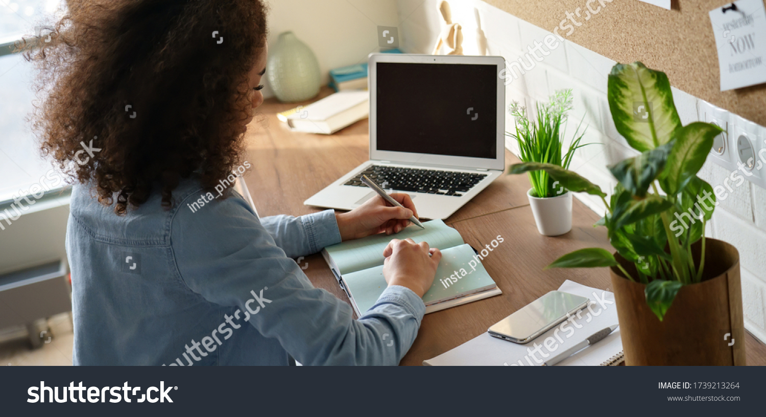 Focused african american teen girl student pupil writing notes in notebook distance learning studying online makes goals check list at home office. Remote college school education, elearning concept. #1739213264
