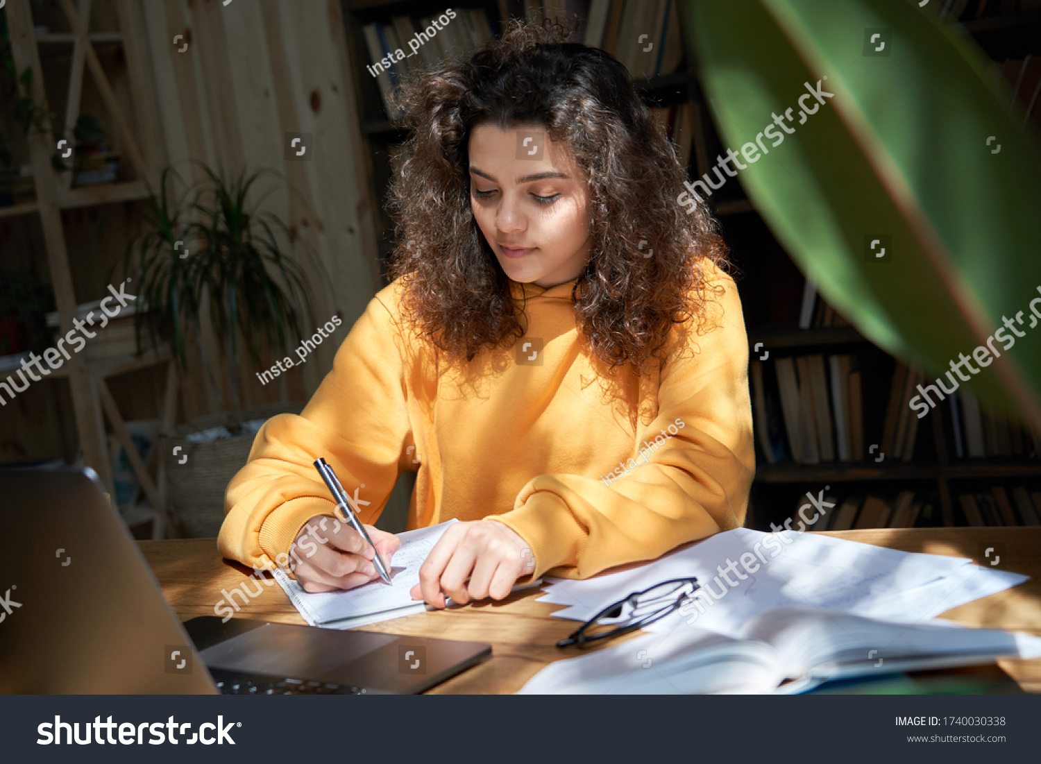 Hispanic teen girl college student study from home office making notes doing homework in sunny room. Latin smart teenage school pupil learning online on laptop sit at desk. Distance elearning concept. #1740030338