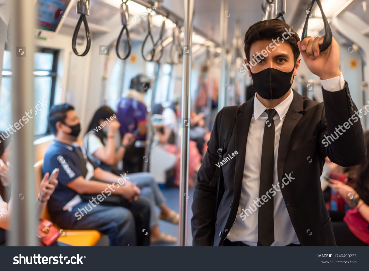 Portrait of confident businessman in black suit wear mask in city finding job during corona crisis using smartphone travelling on empty train #1740400223