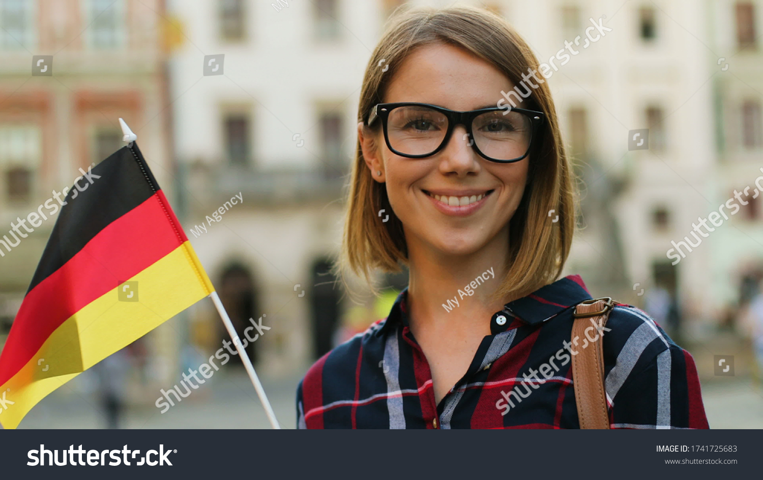 Caucasian woman in casual shirt with german flag posing on camera and smiling on the city street background. #1741725683