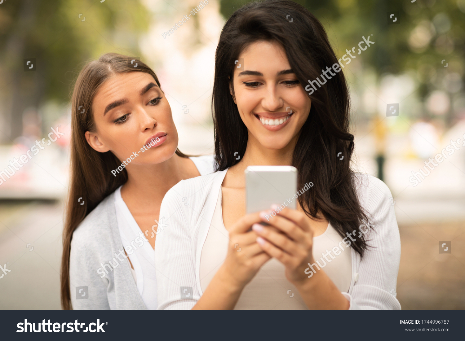 Jealous Friend. Envious Girl Peeking At Girlfriend's Phone While She Texting Walking Together Outdoors #1744996787
