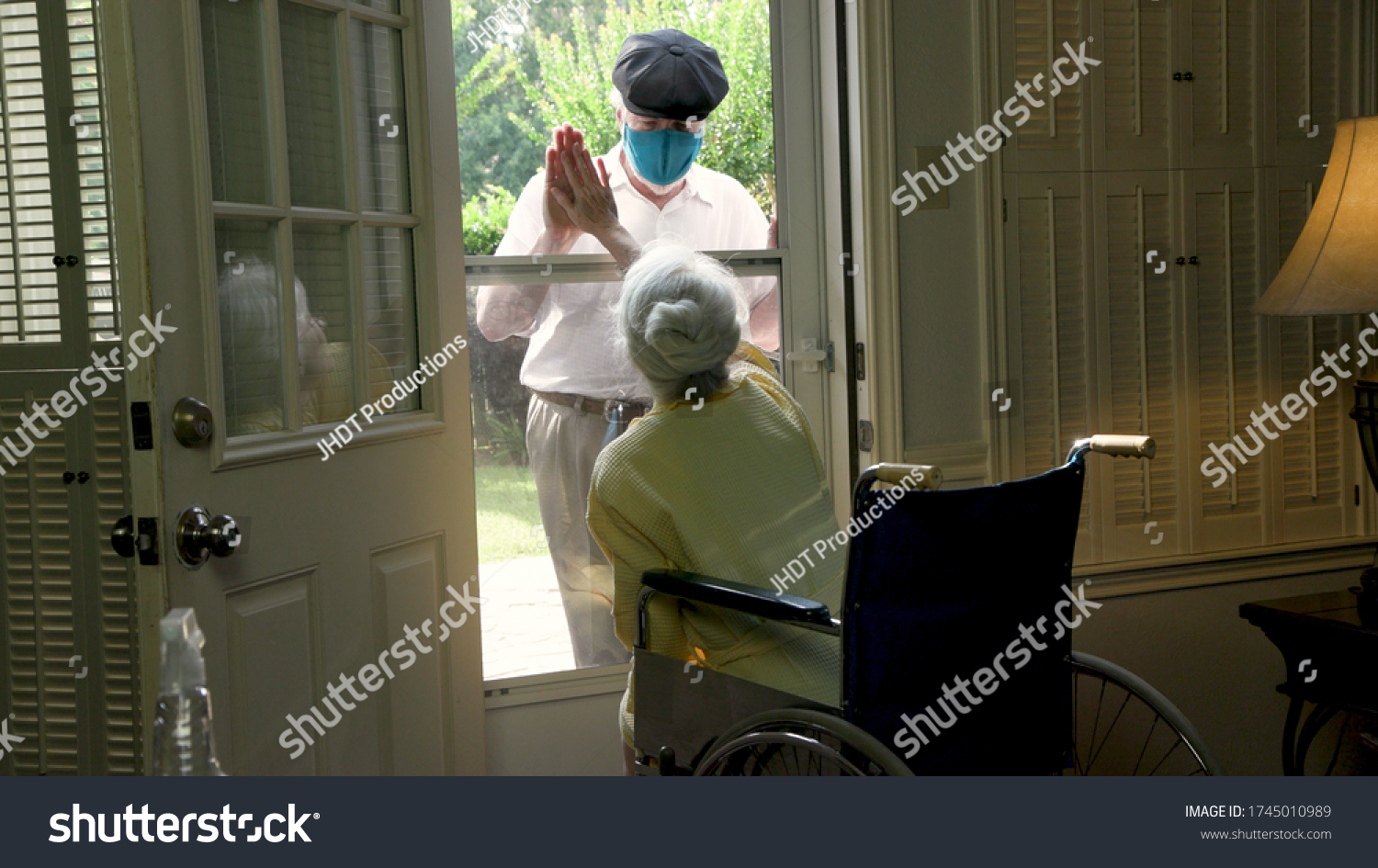 An elderly woman in a wheelchair social distancing because of COVID19 visits with a caring relative or neighbor through her glass storm door. #1745010989