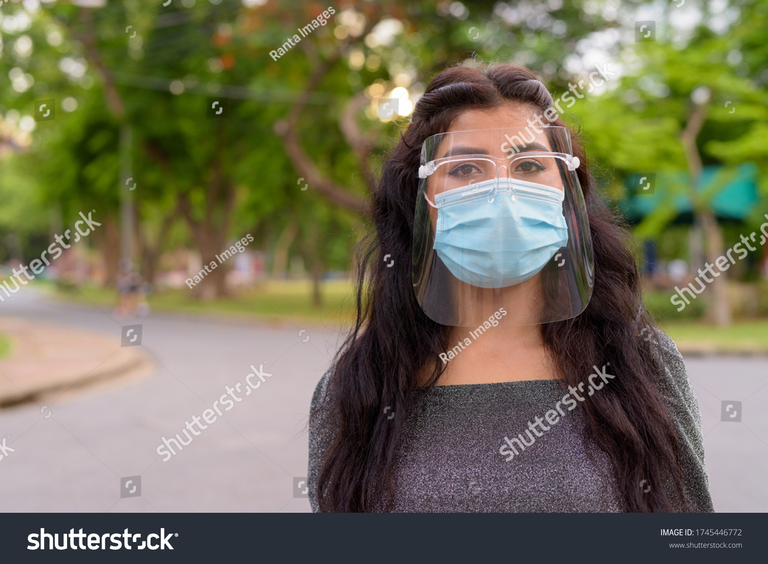 Face of young Indian woman wearing mask and face shield at the park outdoors #1745446772