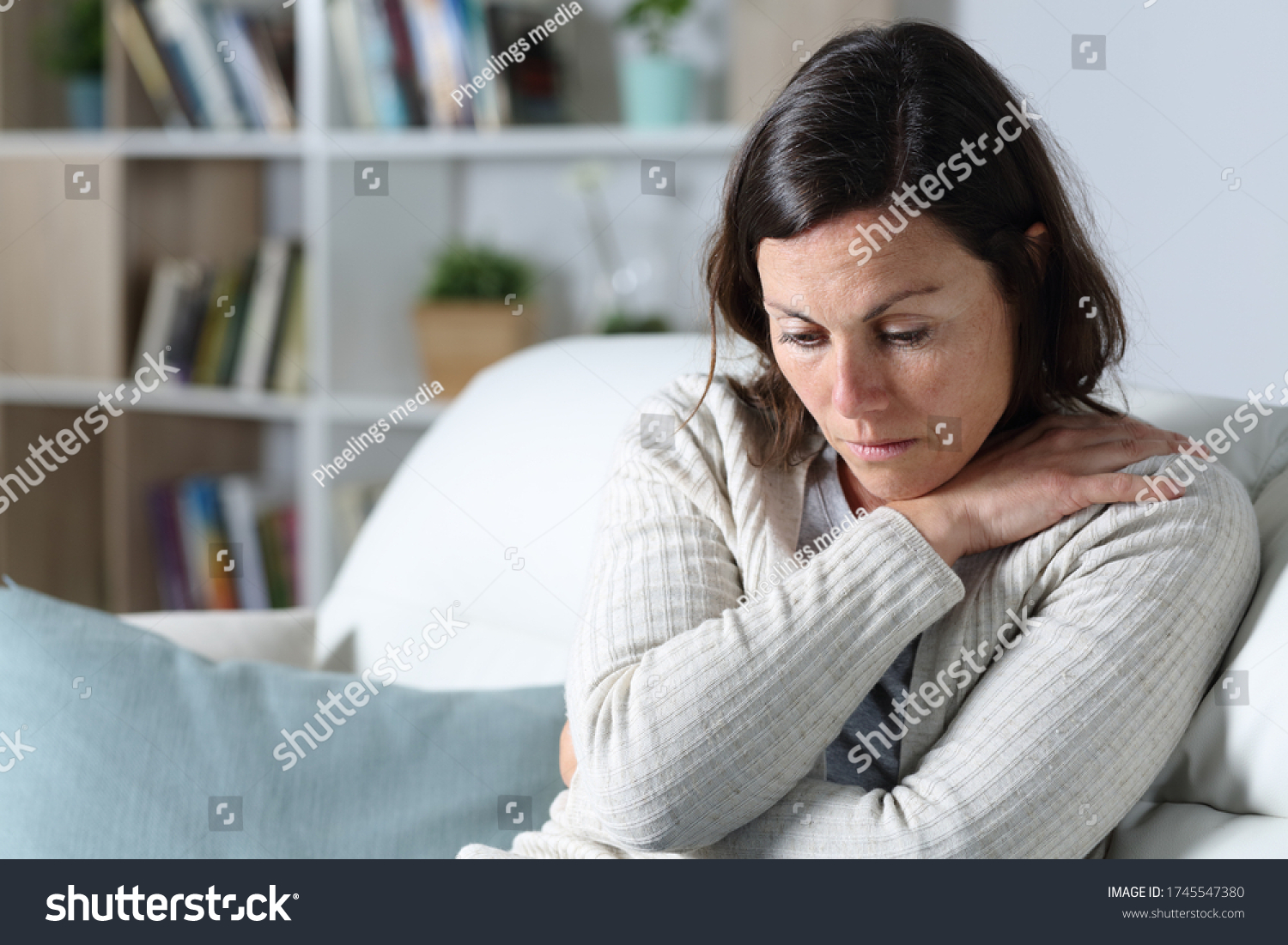 Sad pensive middle age woman looking down depresed sitting on the sofa in the living room at home #1745547380