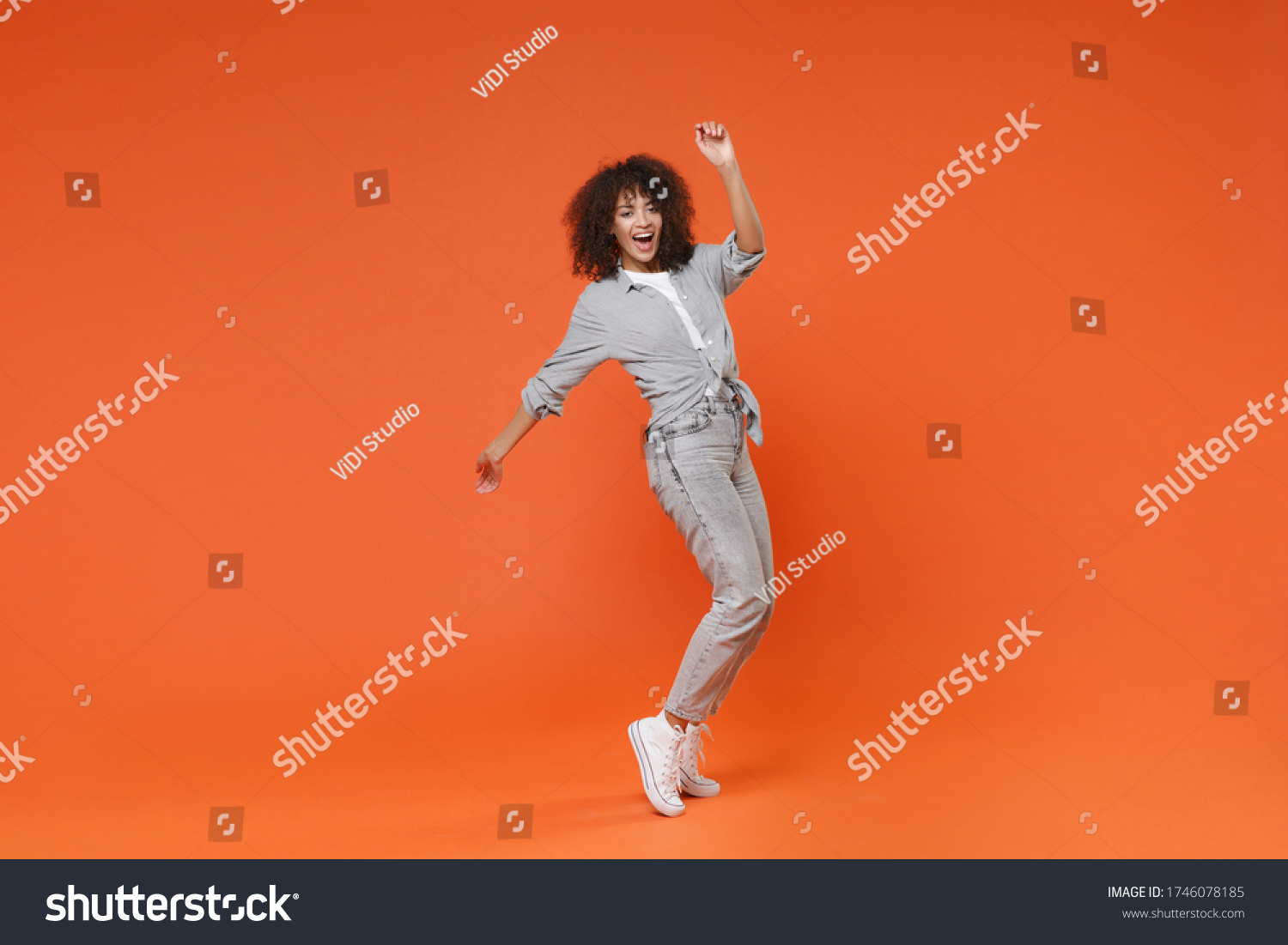 Funny young african american woman girl in gray casual clothes posing isolated on orange background in studio. People lifestyle concept. Mock up copy space. Dancing, standing on toes, rising hands #1746078185
