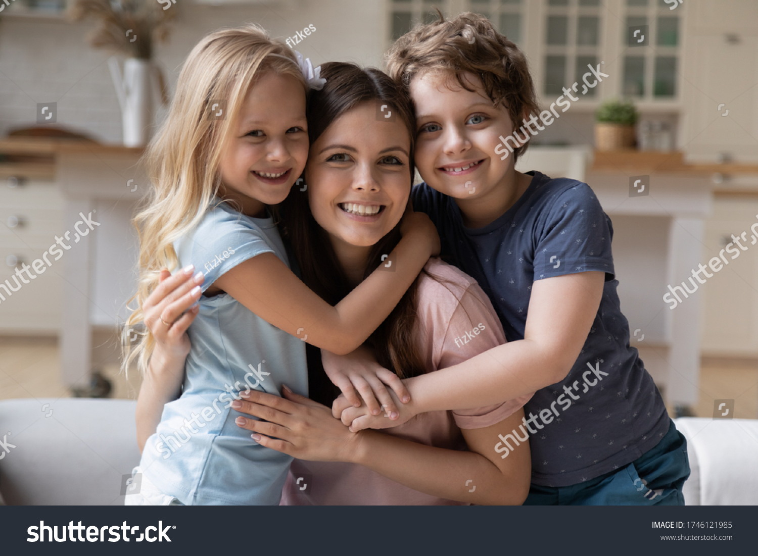 Portrait of happy young mother hug cuddle with smiling little children relax on weekend at home, smiling overjoyed small kids embrace mom or nanny show love and gratitude, family bonding concept #1746121985
