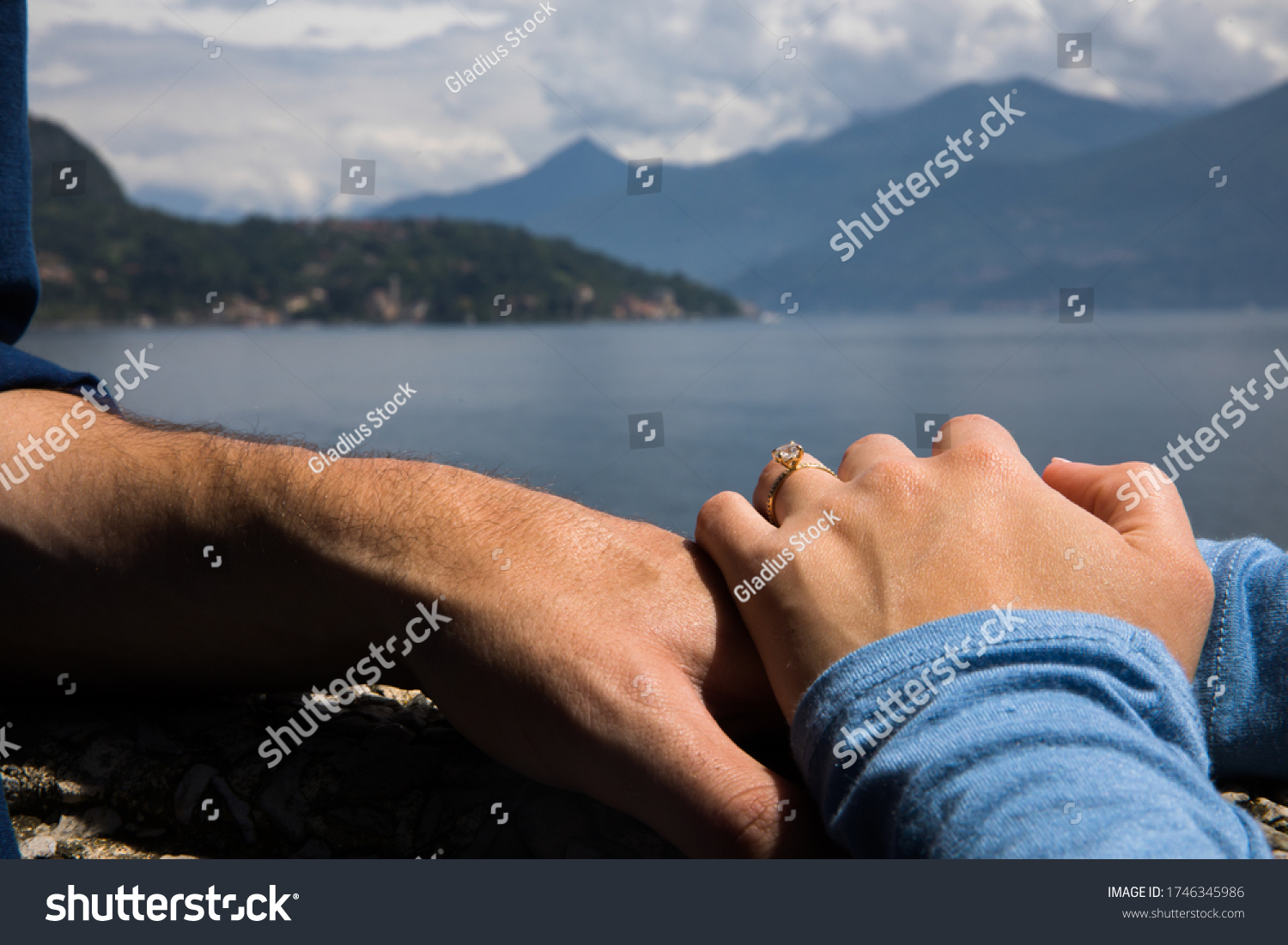 Couple. You can see the hands touching each other. Sensually.Water and mountains in the background.