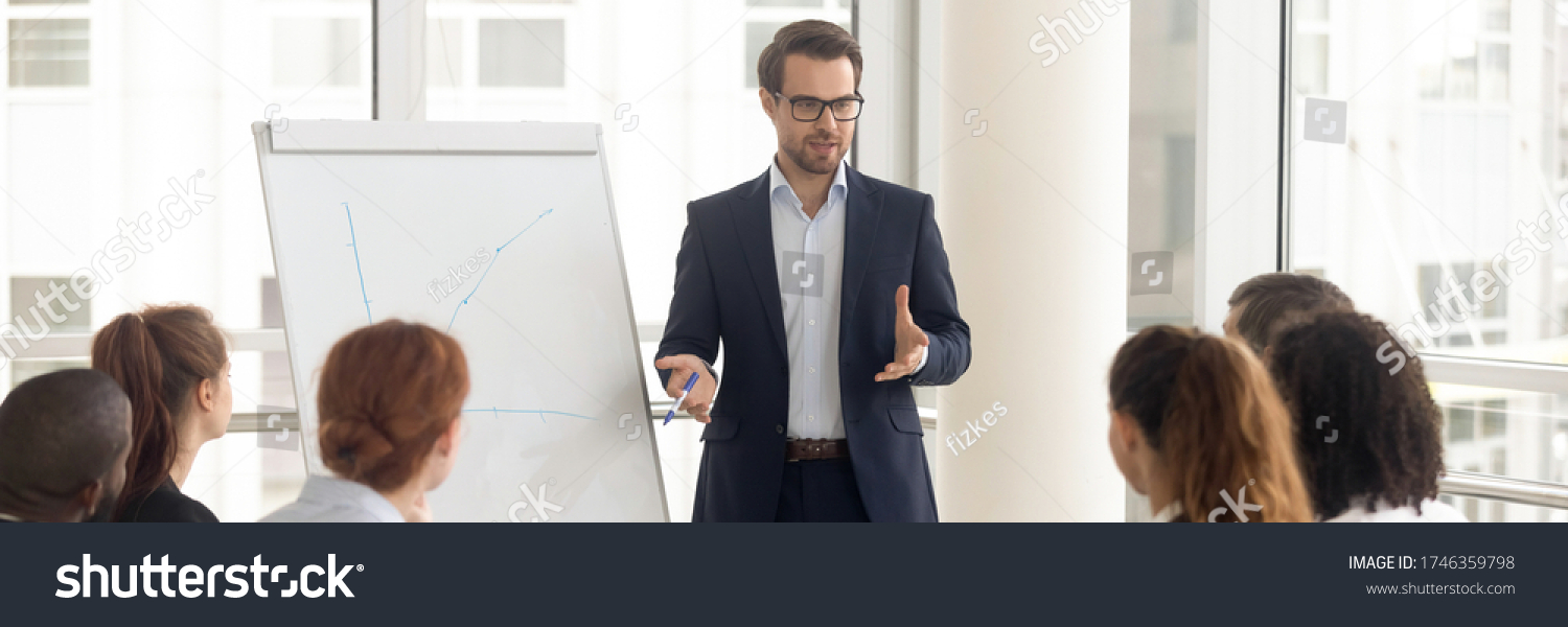 Speaker talking to audience makes presentation using flip chart interacts with group of staff employees, corporate seminar, training activity concept. Horizontal photo banner for website header design #1746359798