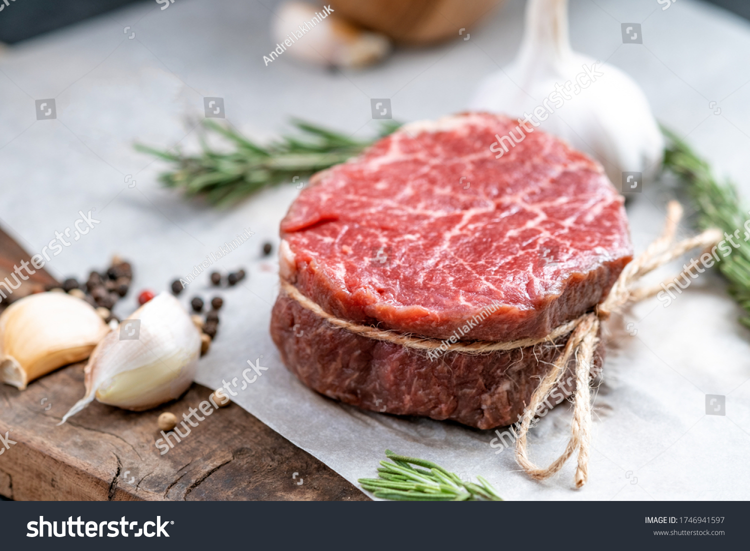 Raw beef filet Mignon steak on a wooden Board on paper with ingredients for grilling, close up #1746941597