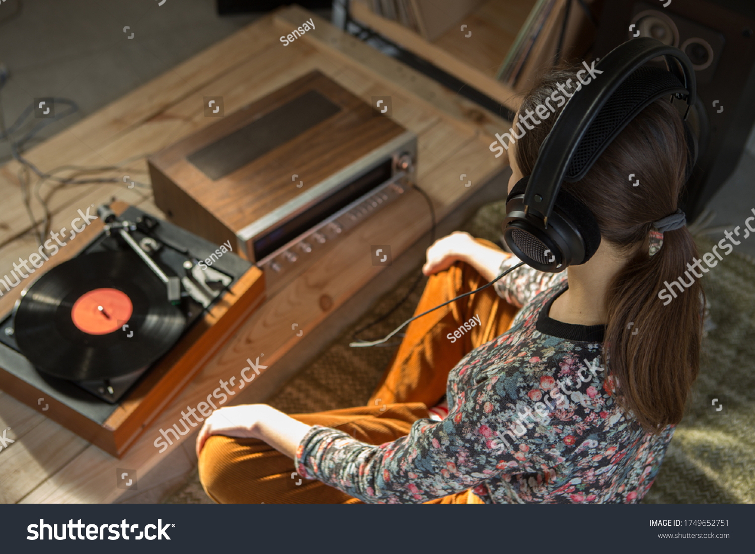 Young Woman listening a music on a HiFi system with turntable, amplifier, headphones and lp vinyl records in a listening room #1749652751