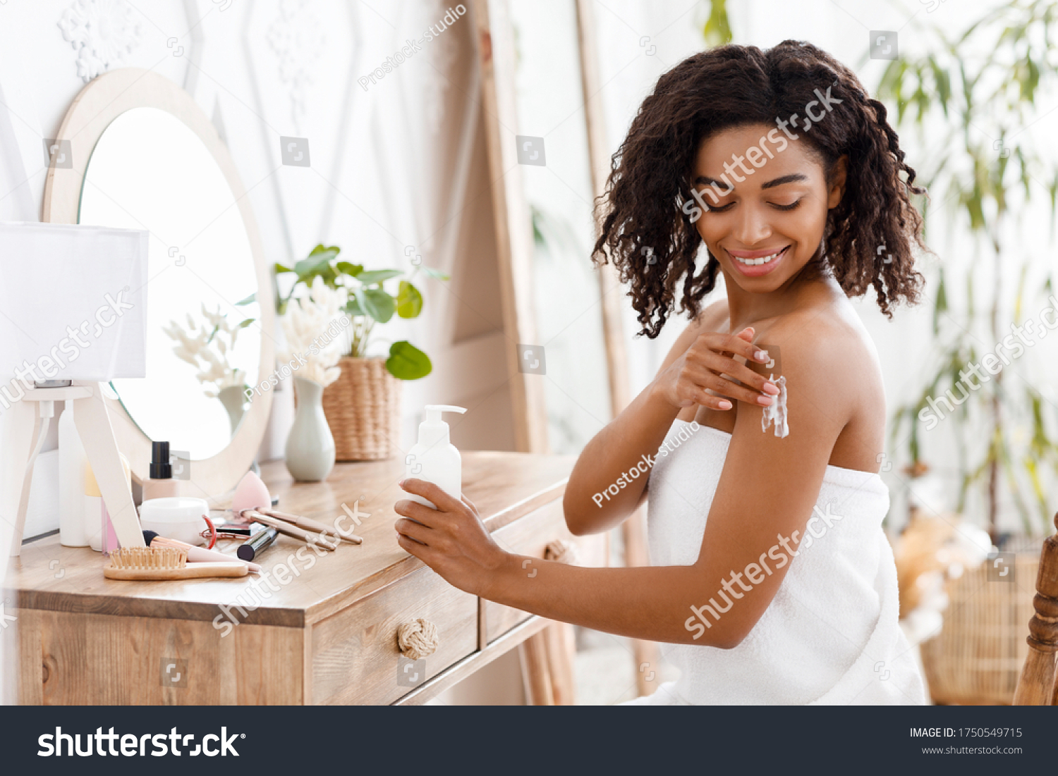 Skin Nutrition. Smiling Attractive Black Woman In Towel Applying Body Lotion, Pampering Herself After Bath, Sitting Wrapped In Towel At Dressing Table #1750549715