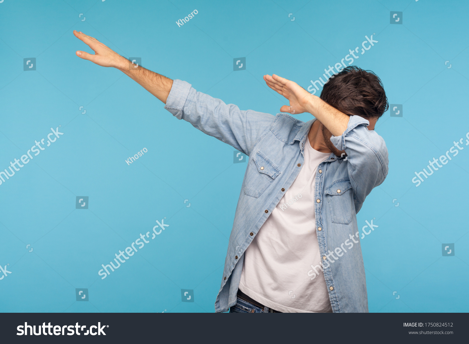 Dab dance. Portrait of man in denim shirt making dabbing movement, famous internet meme of success victory, expressing happiness and following trends. indoor studio shot isolated on blue background #1750824512