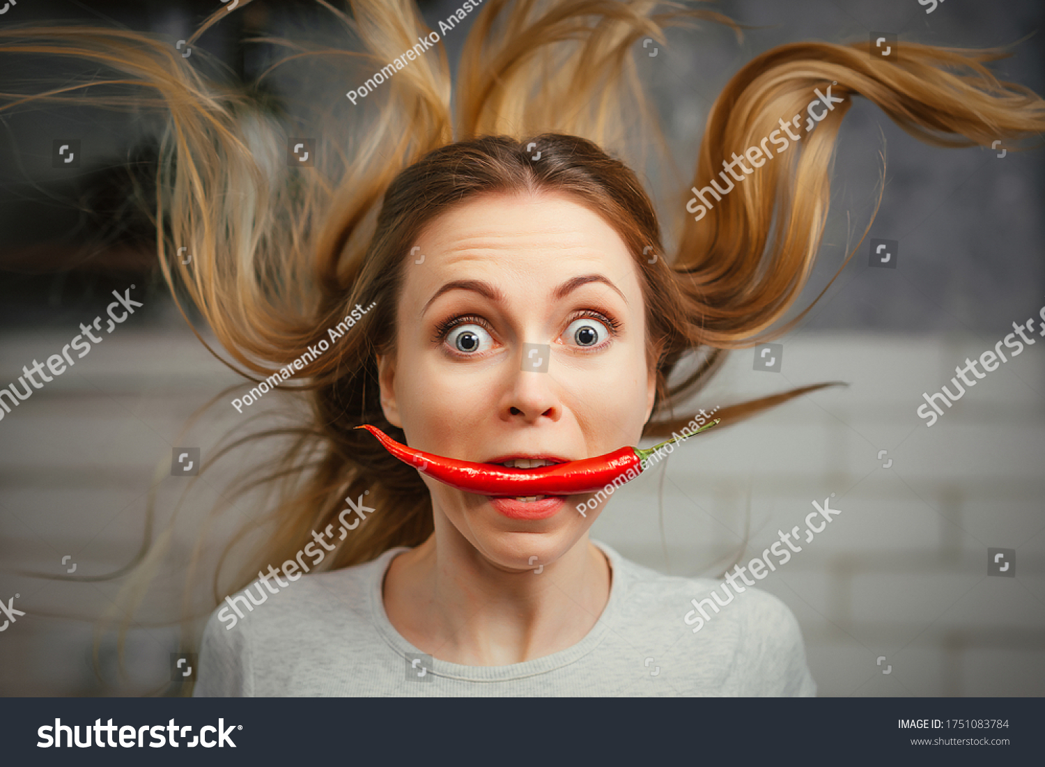A girl with a red hot pepper in her teeth. Chili for cooking. The spicy seasoning is very stinging in the mouth. My hair stood on end. Bite the pepper and get burned. Emotional woman. #1751083784
