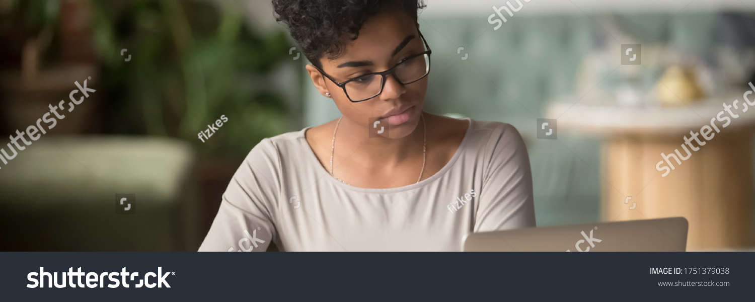 Horizontal photo banner for website header design, African student girl wear glasses sit indoors look at pc screen study on-line, do assignment, prepare for university admission exams, e-study concept #1751379038