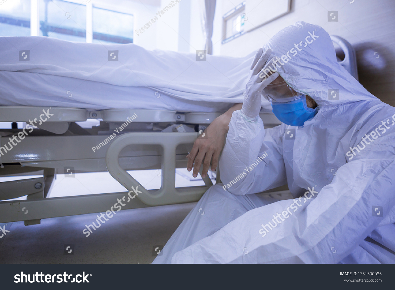 Doctor in protective suit, sadness and depressed beside Coronavirus victim body on bed after the death of patient. #1751590085
