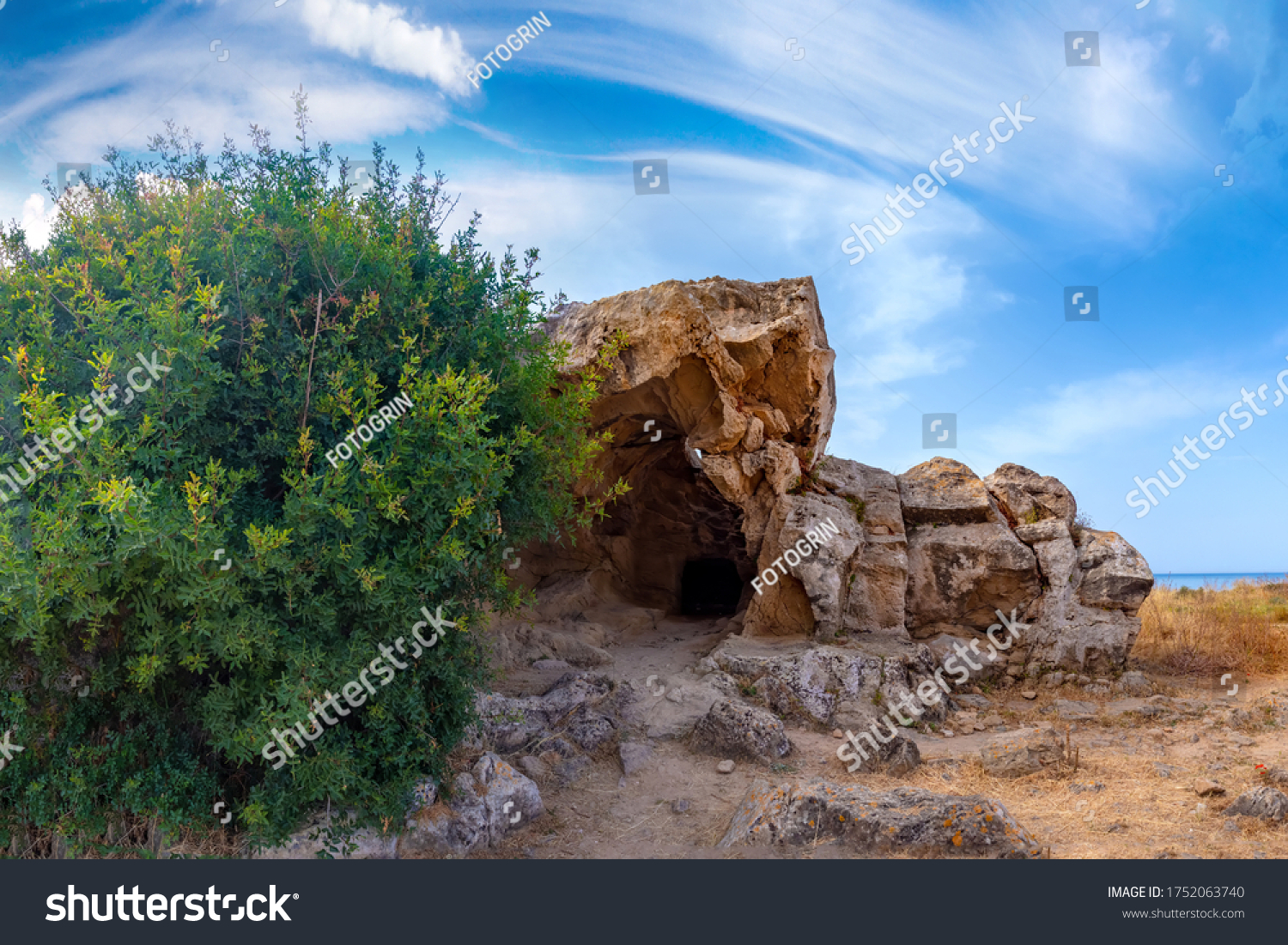 Pathos. Cyprus. Cave in the Archaeological Park of Paphos. Cyclops Cave. Tombs Of The Kings in Cyprus. Tree grows next to cave. Paphos nature landscape. Archaeological Park in open. #1752063740