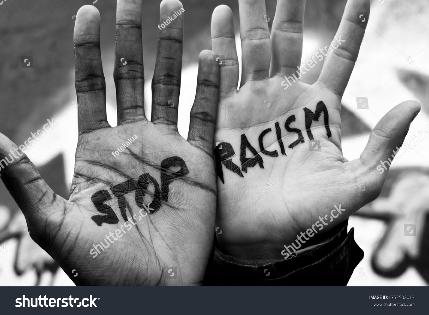 Close-up of the raised hands of two men of different ethnicity with the slogan "stop racism" written on their palms. Black and white anti racism image. #1752502013