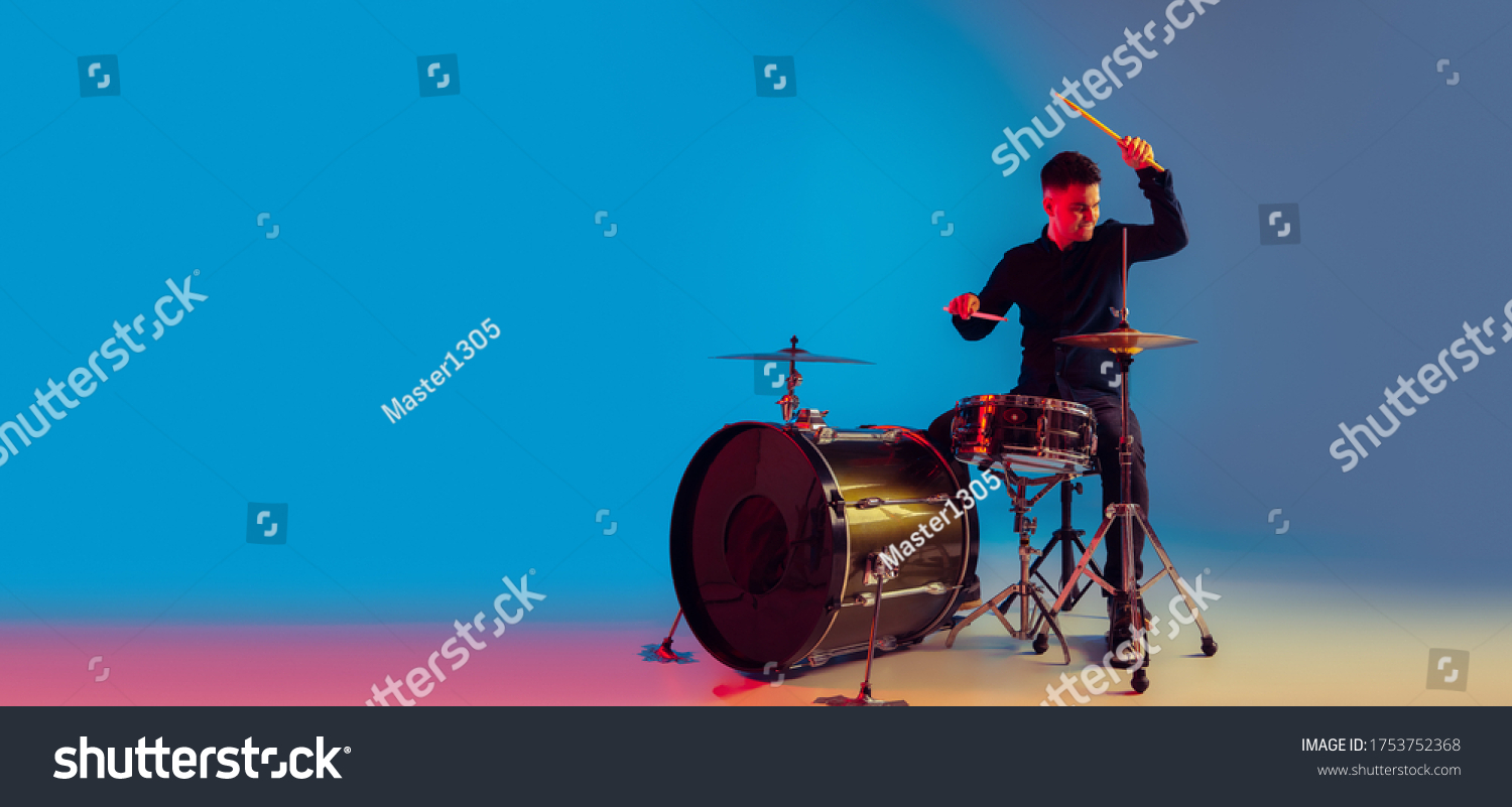 Caucasian male drummer improvising isolated on blue studio background in neon light. Performing, looks inspired, energy. Concept of human emotions, facial expression, ad, music, art, festival. Flyer. #1753752368