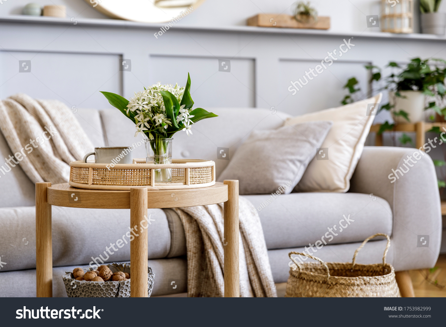 Scandinavian living room interior with design grey sofa, wooden coffee table, plants, shelf, spring flowers in vase, decoration and elegant personal accessories at home decor. #1753982999