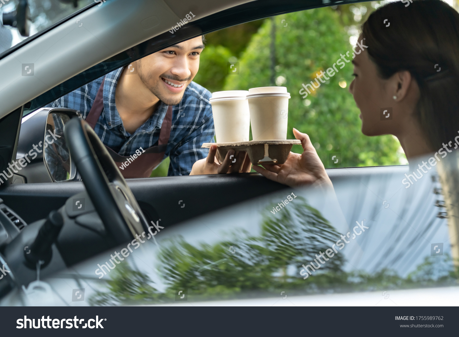 Waiter giving hot coffee cup with disposable tray and bakery bag through car window to customer at drive thru service station. Drive thru is popular service after coronavirus covid-19 pandemic. #1755989762