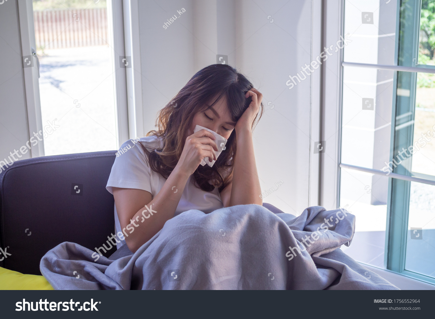 An Asian woman sick on the sofa in the house. Women have headaches, high fever and runny nose due to flu. The concept of illness with influenza #1756552964