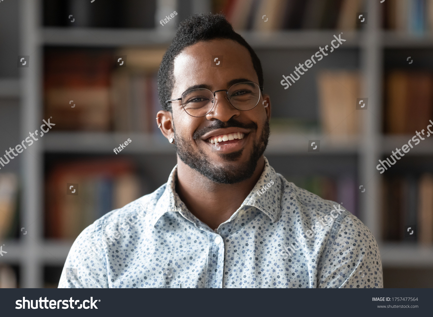 Head shot of african american bearded guy with pierced ear casual shirt smiling looking at camera standing indoor. Webcam view, conference video call, confident company representative portrait concept #1757477564