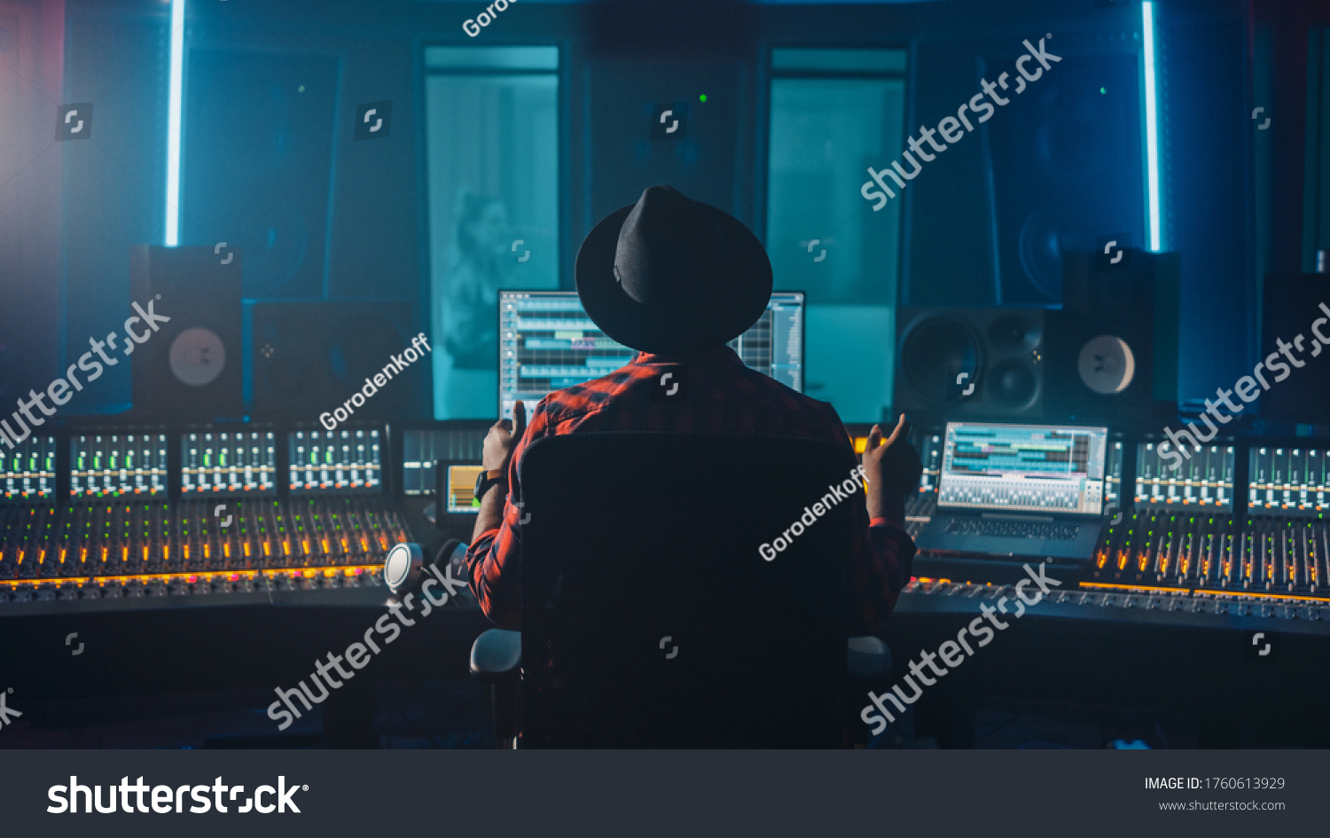 Producer, Audio Engineer Uses Control Desk for Recording New Album Track in Music Record Studio, in the Soundproof Room Musician, Artist, Performer Sings a Song from New Album. Back View #1760613929