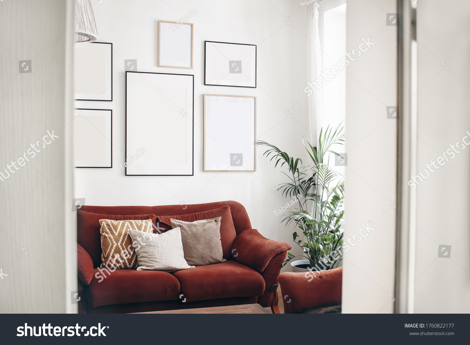 Blank picture frames mockups on white wall. White living room design. View of  modern boho, scandi style interior with sofa, cushions, potted palm plant through open white door. Home staging concept. #1760822177