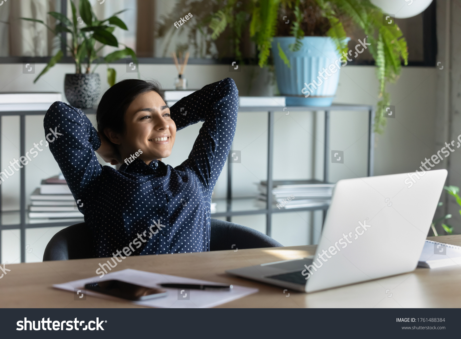 Carefree indian employee resting after busy fruitful workday leaned on office chair puts hands behind head feels satisfied by work done, achievements, job promotion, looking in distance out the window #1761488384