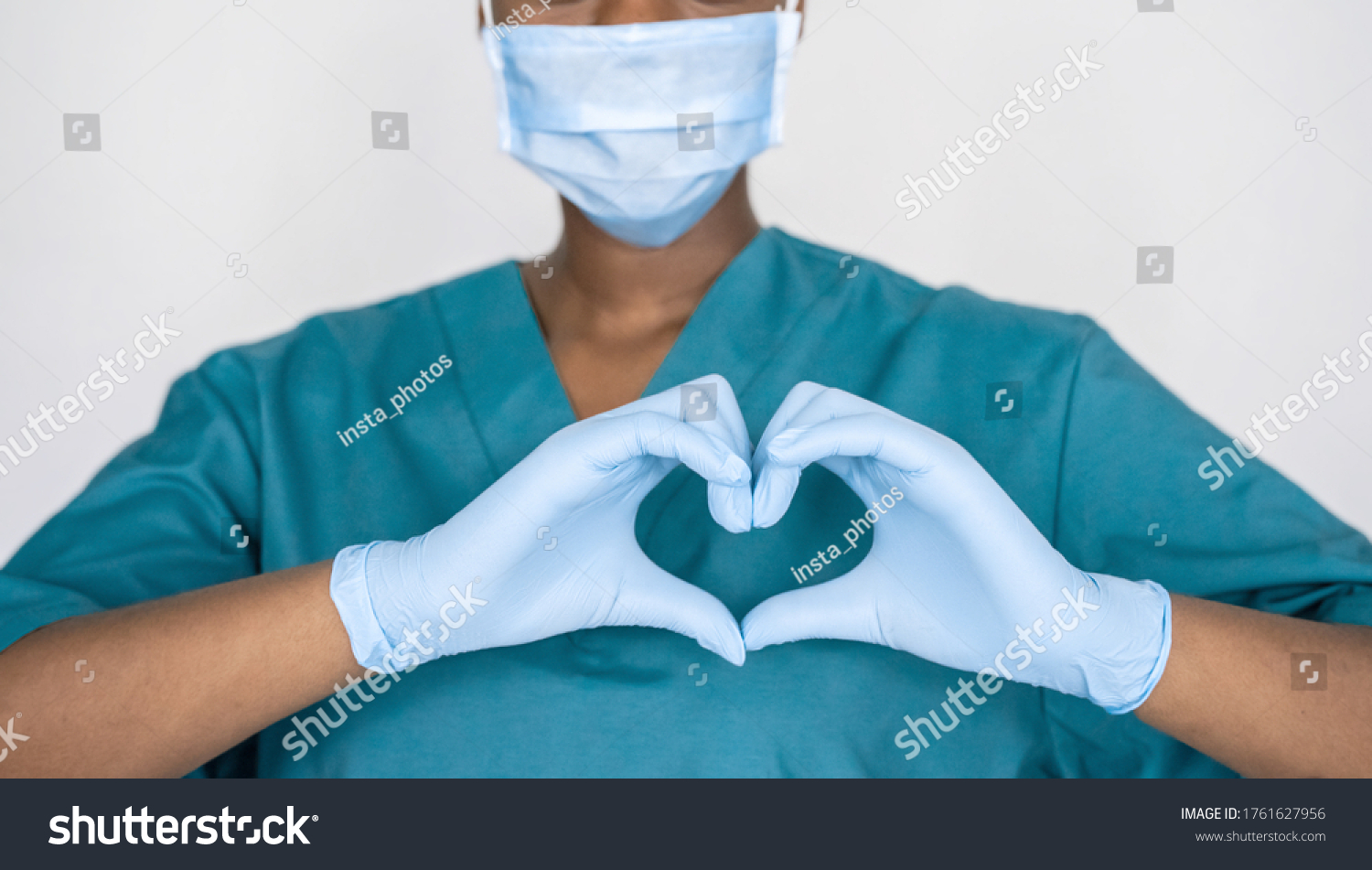 Female african professional medic nurse wear face mask, gloves, blue green uniform showing heart hands shape. Medical love, care and safety symbol, corona virus health protection sign concept. Closeup #1761627956