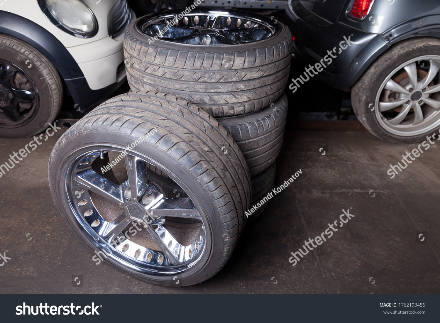 A set of expensive stylish winter tires for a German car with chrome wheels in the garage against the background of cars stored in the summer season, spare wheels. #1762193456