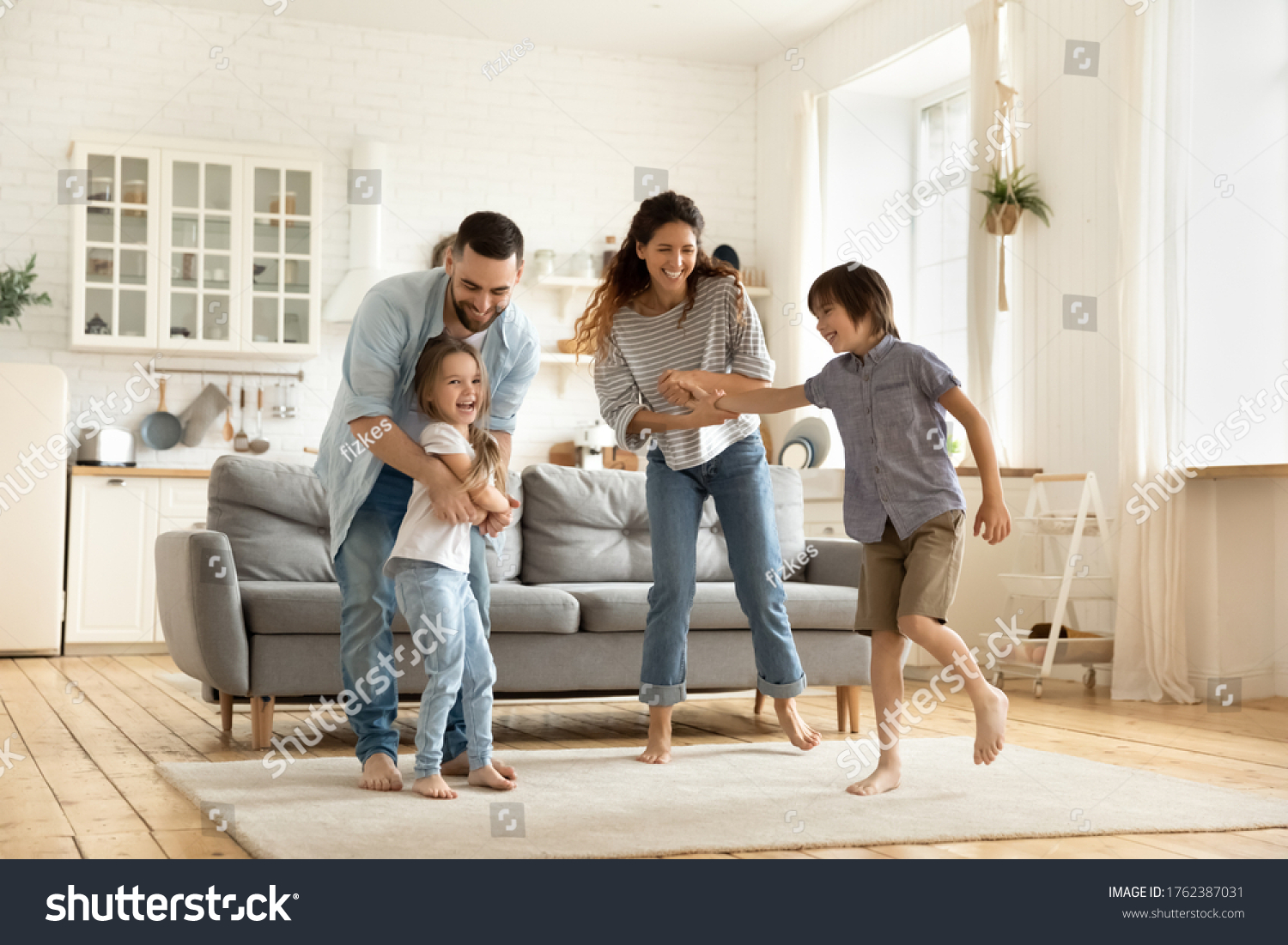 Happy family playing funny game having fun together with little son and daughter in modern living room. Young dad and mother with adorable cute children doing exercises, enjoying weekend at home. #1762387031