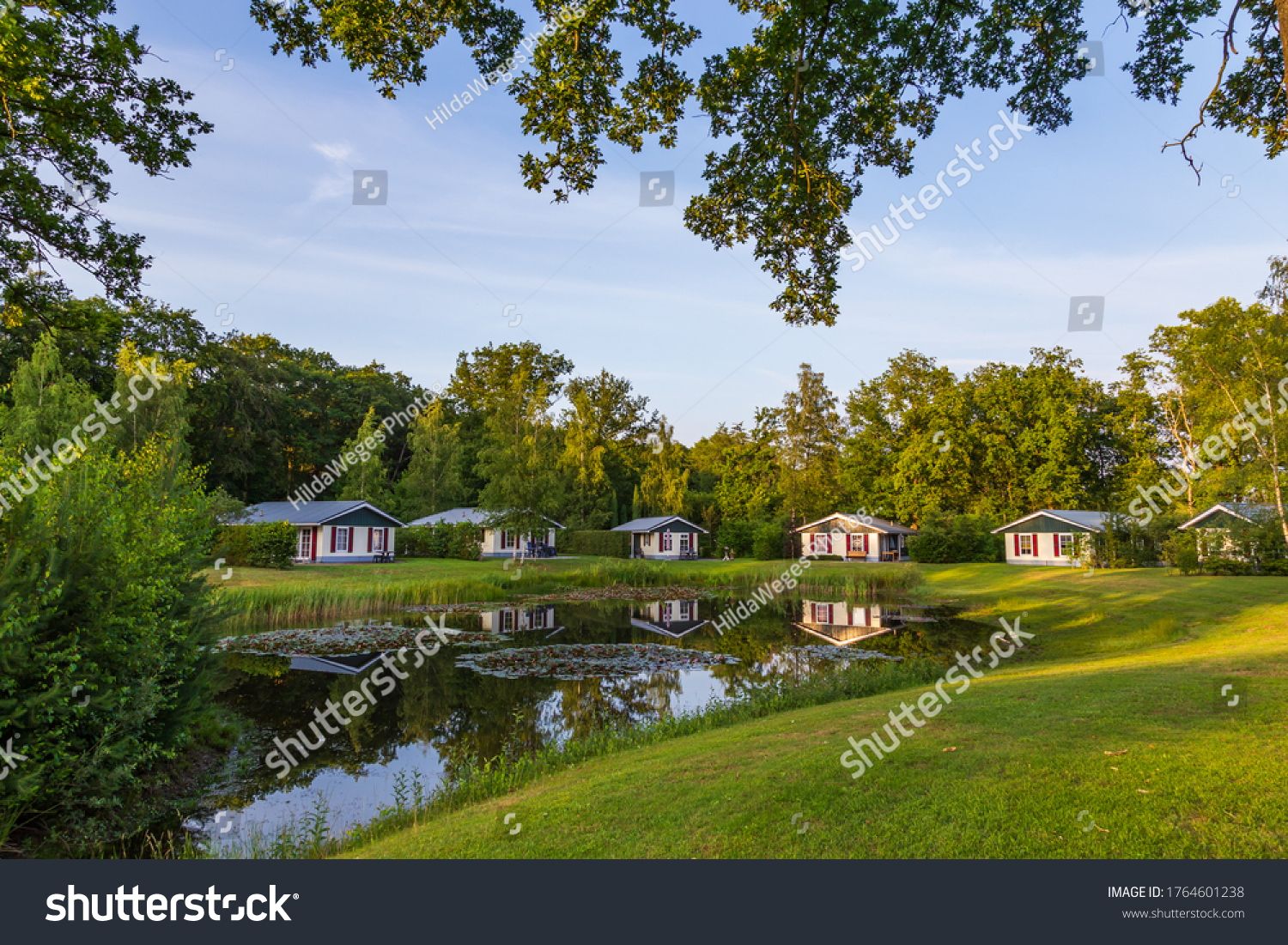 Row of colorful wooden vacation home reflected in a pond at recreation park in the middle of nature in the Netherlands #1764601238