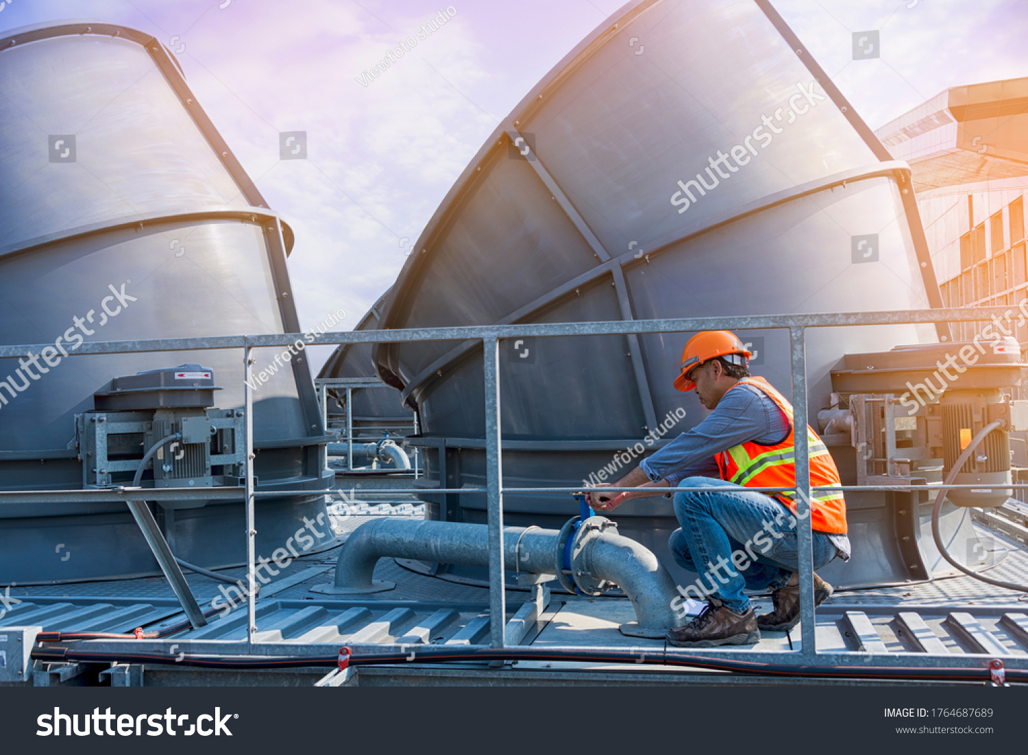 worker open valve of cooling tower on blue sky background. worker opening butterfly valve on top of cooling Tower. worker check valve on cooling tower. #1764687689