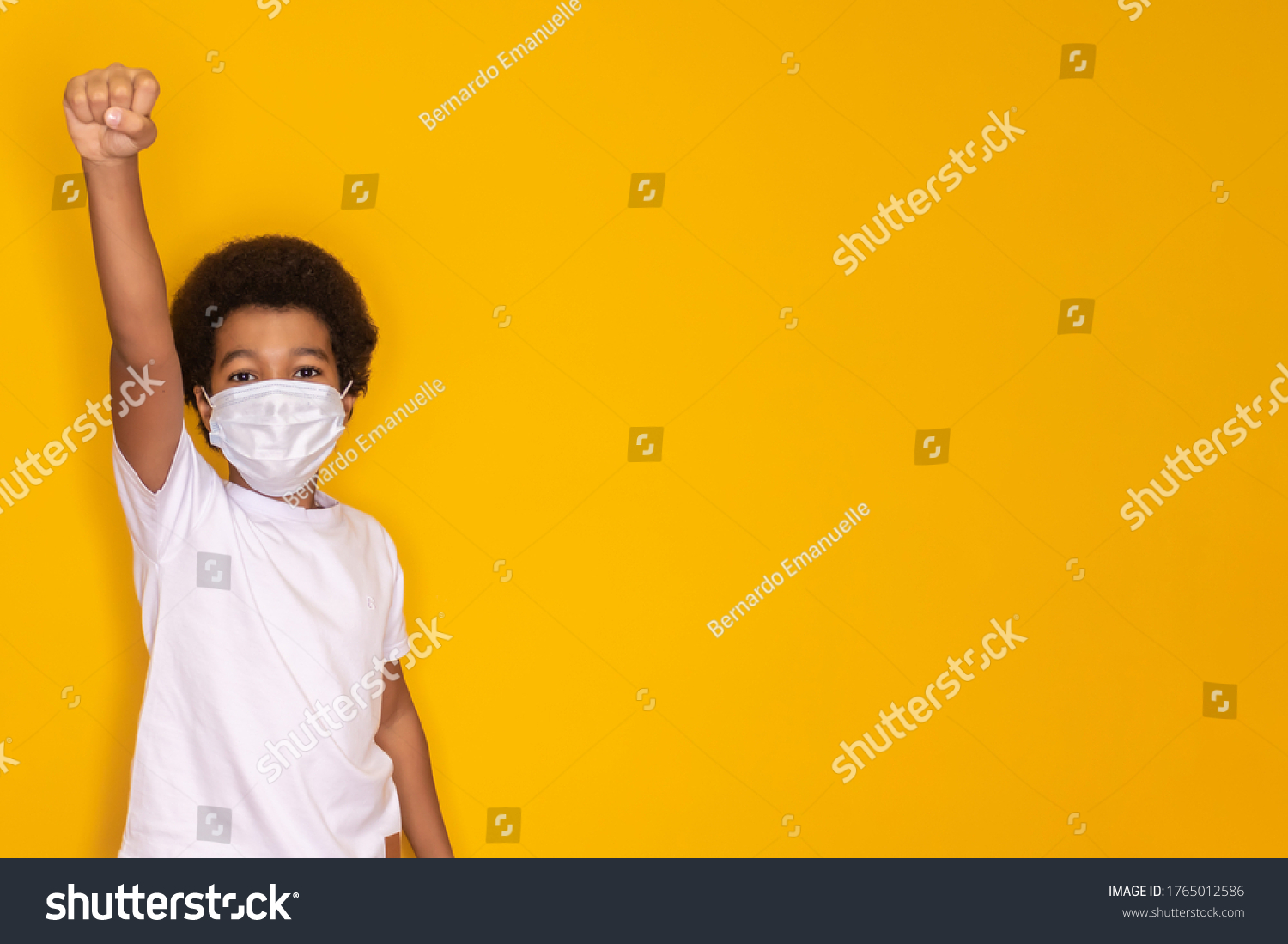 Portrait of little afro boy with medical face mask looking at camera. Child wearing protective mask from virus . Coronavirus and pandemic concept. Kid in hero pose with mask #1765012586