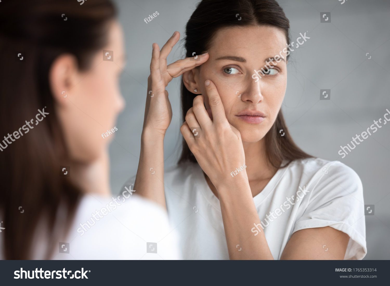 Anxious young woman look in the mirror worried about wrinkle or acne on unhealthy skin, upset unhappy millennial female examine squeeze pimple on face, cosmetology, skincare concept #1765353314