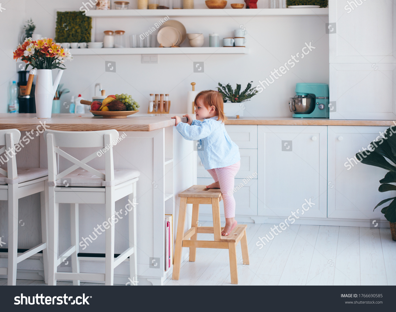 curious infant baby girl trying to reach things on the table in the kitchen with the help of step stool #1766690585