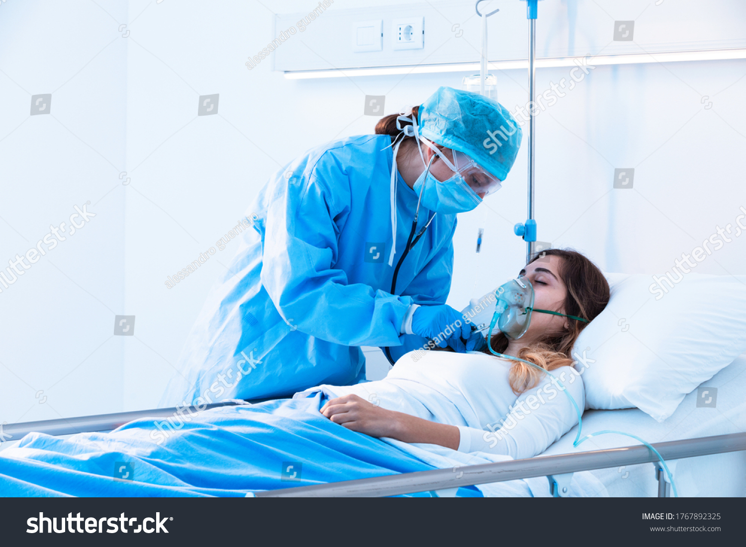 Doctor examining female patient in critical health conditions using a stethoscope in the intensive care unit of a modern hospital during covid-19 pandemic #1767892325