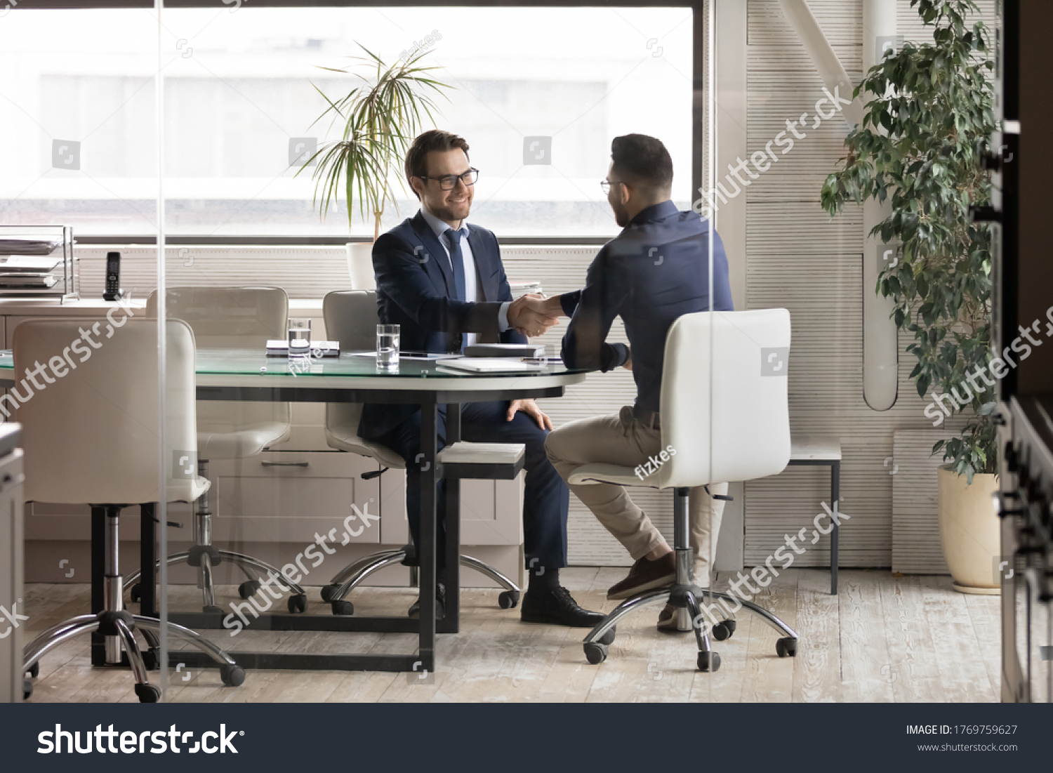 Smiling multiracial young businessmen handshake greeting get acquainted at boardroom briefing, excited diverse male business partners shake hands make agreement after successful office negotiations #1769759627