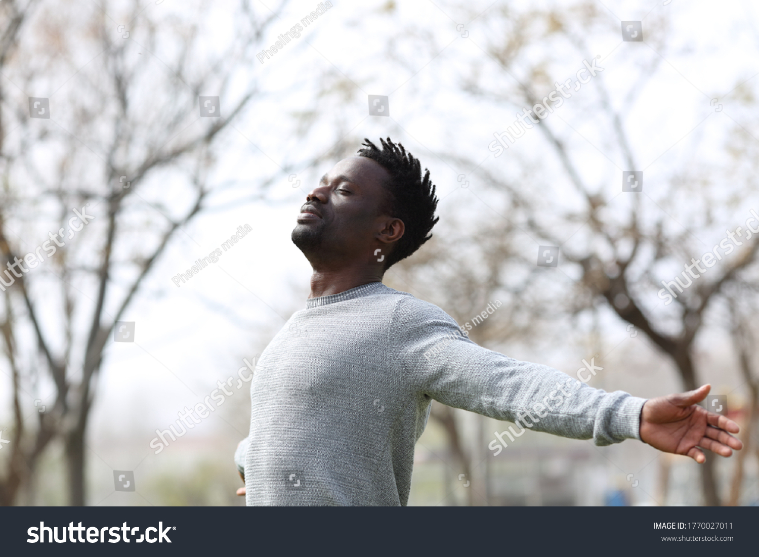 Satisfied black man breathing fresh air with eyes closed standing in the park outdoors  #1770027011