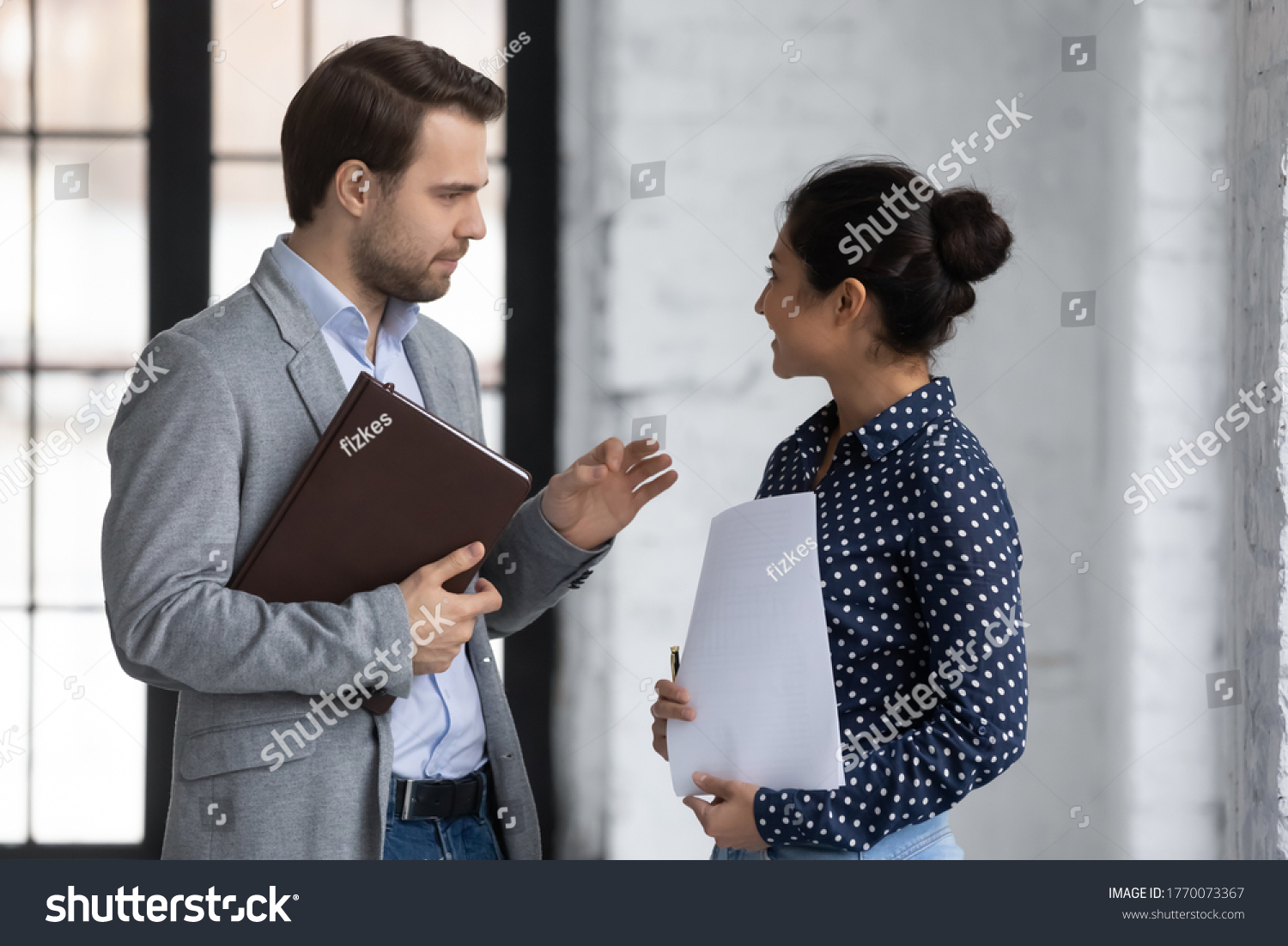 Diverse office workers colleagues met standing in office and talking, friendly Indian woman communicates with Caucasian man discussing project ideas, 2 executives having pleasant conversation concept #1770073367